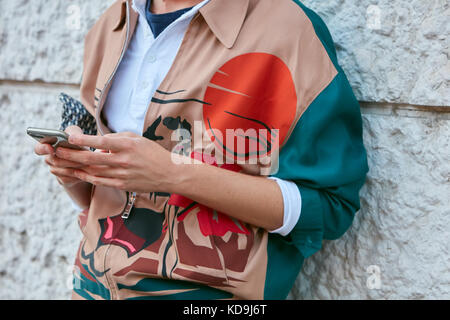 MILANO - 21 SETTEMBRE: Uomo con bomber in beige, verde e arancione che guarda lo smartphone prima della sfilata Prada, Milano Fashion Week Street sty Foto Stock