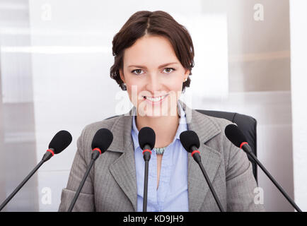 Sorridente imprenditrice holding parlando della carta nella parte anteriore di più microfoni Foto Stock