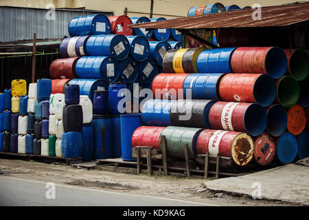 Utilizzate i fusti di olio alta impilati in un commercio all'ingrosso di olio fornitori drum store sul ciglio della strada. riciclato gallone tamburi di plastica e contenitori di acqua di line road Foto Stock