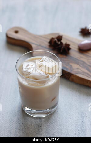 Tè dolce tailandese speziato con anice stellato con latte condensato su vetro con cubetti di ghiaccio. Tagliere e stella sullo sfondo Foto Stock