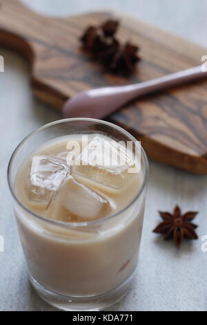 Tè dolce tailandese speziato con anice stellato con latte condensato su vetro con cubetti di ghiaccio. Tagliere e stella sullo sfondo Foto Stock