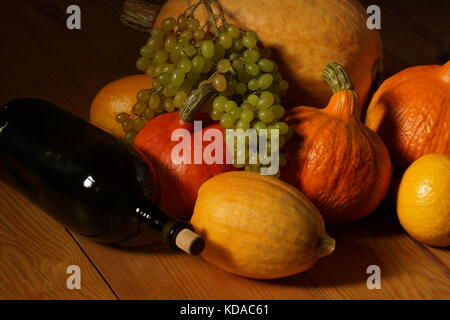 Raccolto autunnale di zucche e uva e una bottiglia di vino sul pavimento di una casa in paese. Foto Stock