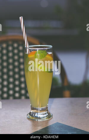 La limonata bicchiere alto con calce e fettine di arancia, foglie di menta e paglia colorata, sedia vintage in background Foto Stock