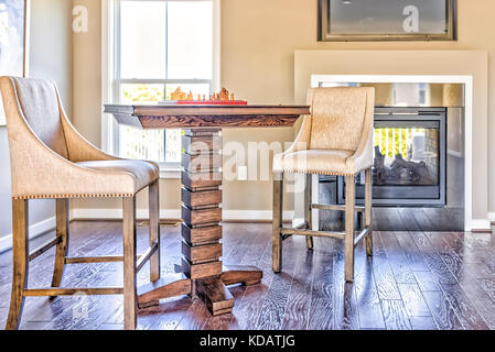 Primo piano della scacchiera tavolo con pezzi di legno nella luce del sole su soppalco di casa con camino e sedie Foto Stock