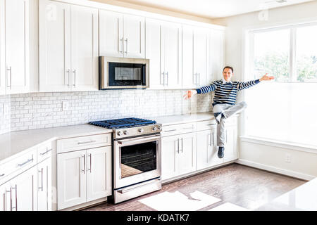 Giovane uomo seduto sul bancone della cucina con tese le braccia aperte in pulito, moderno, bianco di design per la casa Foto Stock