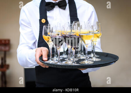 Professional cameriere in nero uniforme che serve vino rosso e bianco. Servizio di catering è servire il vino e il succo su un piatto a parte di affari o eventi aziendali par Foto Stock