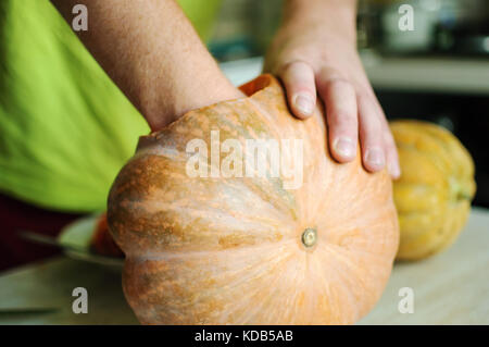 Zucca di Halloween processo di taglio, maschio le mani prendere fuori i semi e gli avanzi di zucca. messa a fuoco selettiva e bokeh di fondo. Foto Stock