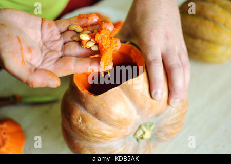 Zucca di Halloween processo di taglio, maschio le mani prendere fuori i semi e gli avanzi di zucca. messa a fuoco selettiva e bokeh di fondo. Foto Stock