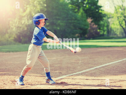 Ragazzo di colpire la sfera mentre a giocare a baseball in uniforme blu Foto Stock