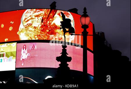 Digital commerciale / marketing / schermi pubblicitari illuminati fino a Piccadilly Circus di Londra con una silhouette dell'Angelo statua di Anteros sullo schermo Foto Stock