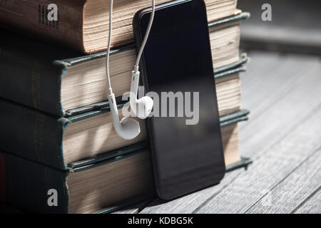 Il libro, gli auricolari di grandi dimensioni giacciono su un sfondo di legno, audiolibri Foto Stock