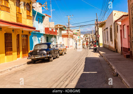 Scena di strada di un vecchio American automobile parcheggiata esterno colorato stile coloniale case sulla strada di ciottoli, Trinidad, Cuba, Caraibi, Foto Stock