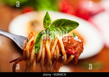 Forcella con spaghetti basilico e Polpetta con piastra in distanza. Foto Stock