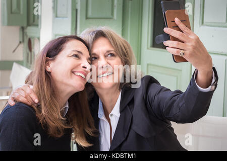 Un senior donna, 61, prendendo un selfie con il suo cellulare insieme con il suo 46 anni vecchio amico, il concetto di stile di vita. Foto Stock