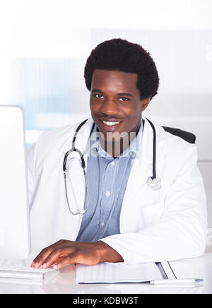 Ritratto di Felice medico con stetoscopio seduti ad una scrivania Foto Stock