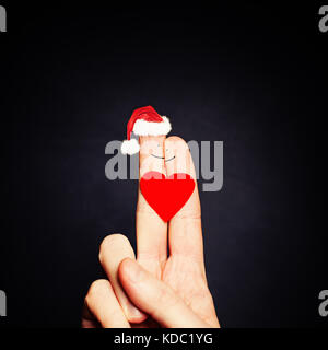 Natale giovane. felice coppia dita in santa hat con cuore Foto Stock