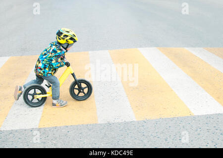 Un ragazzo con una bicicletta attraversa un passaggio pedonale con contrassegni di colore giallo Foto Stock