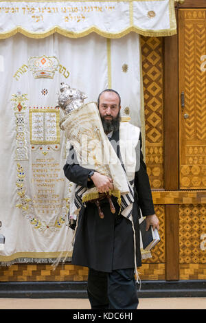 Una religiosa ebraica uomo che porta un rotolo di Torah dall'arca santa il luogo in cui esso verrà letta. In Brooklyn, New York. Foto Stock