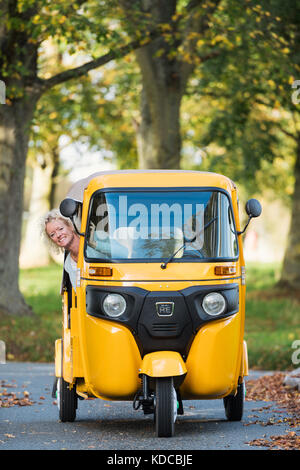 Una donna bionda che aziona un giallo tuk tuk in un villaggio inglese Foto Stock