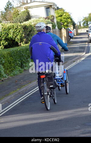 Un centro di età o ritirato l uomo e la donna o coppia a cavallo di un ciclo in tandem o in bicicletta lungo la strada sul lungomare a Cowes sull'isola di Wight. Foto Stock