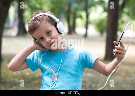 Ritratto di un dolce bambino che mostra piacere mentre ascolti la musica. Egli era in possesso di un telefono cellulare in mano e ascolta la sua musica preferita Foto Stock