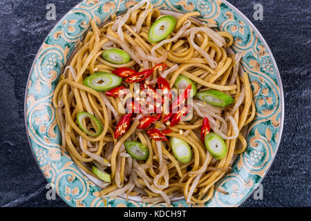 Stile cinese wok mescolare uovo fritto con le tagliatelle beansprouts e il peperoncino rosso su nero ardesia piastrella da cucina Foto Stock