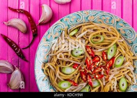 Stile cinese wok mescolare uovo fritto con le tagliatelle beansprouts e il peperoncino rosso su una rosa di sfondo di legno Foto Stock