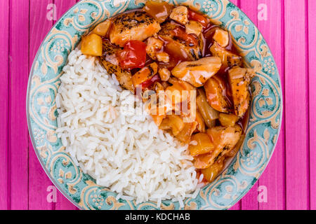 Stile cantonese dolce e aspro di pollo con riso bianco bollito contro una rosa backgroound in legno Foto Stock