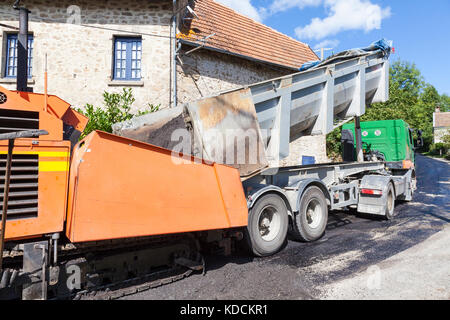 Suggerimento carrello in movimento davanti a una strada tarring macchina con asfalto premix il riempimento della parte anteriore della macchina per lo spandimento sulla superficie della strada nella parte posteriore Foto Stock