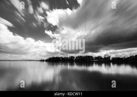 Una lunga esposizione vista di un lago con lo spostamento delle nuvole bianche rispecchiando perfettamente su acqua Foto Stock