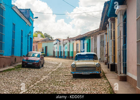 Scena di strada di un vecchio American automobile parcheggiata esterno colorato stile coloniale case sulla strada di ciottoli, Trinidad, Cuba, Caraibi, Foto Stock