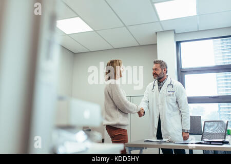 Medico maschio stringono le mani con paziente in clinica. Medical professional meeting donna in ospedale. Foto Stock
