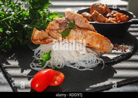 Cellophane vermicelli di riso con fette di salmone alla griglia con pomodoro, cipolla e prezzemolo nel Consiglio di Amministrazione di nero ardesia. Close-up.Il telaio orizzontale. Foto Stock