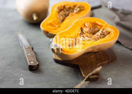 Tagliate a metà la zucca zucca su legno tagliere. coltello e asciugatutto sul calcestruzzo scuro dello sfondo di pietra. bassa angolazione. smoothie, pasto ingre Foto Stock