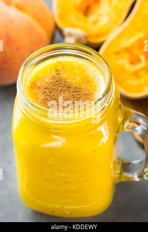 Vaso di vetro con materie vegane zucca zucca smoothie con pesche, banane, torta di spezie. Ingredienti sulla pietra scura. sfondo autunno sano dri Foto Stock