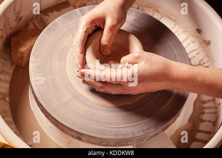 Close-up di una donna splendidamente scolpisce un marrone vaso di argilla su un tornio del vasaio, una vista superiore Foto Stock