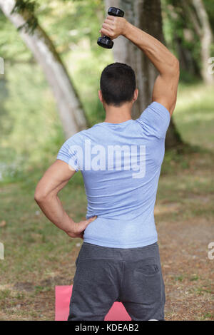 Uomo con braccia alzate facendo esercizi di sollevamento con manubri Foto Stock