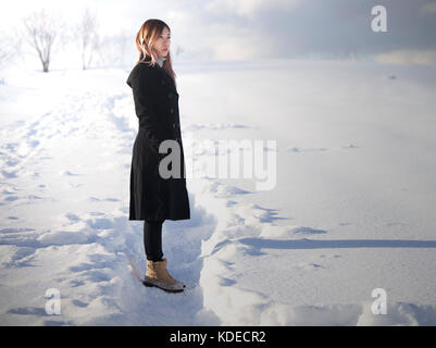 Ragazza asiatica con cappotto nero a Mild Seven Hills, Biei, Hokkaido, Giappone, in inverno, in piedi e guardando lontano Foto Stock