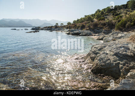 La luce del sole scintillante off un calmo mare mediterraneo sulla costa del deserto des Agriates vicino a St Florent in corsica con cap corse a distanza Foto Stock
