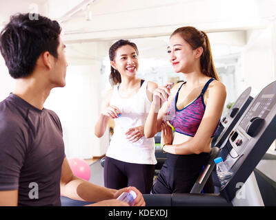 Giovane uomo asiatico e donne chiacchierando in palestra mentre prendendo una pausa. Foto Stock