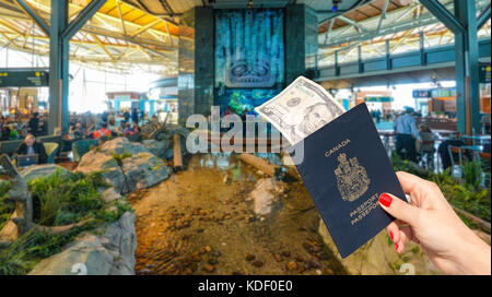 Aeroporto Internazionale di Vancouver - 11 aprile, 2017: a mano in possesso di un passaporto canadese con un $5 nota all'aeroporto internazionale di Vancouver lounge. Foto Stock