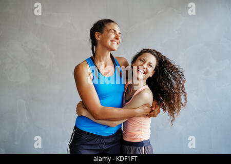 Due giovani donne in abbigliamento sportivo di ridere e di stare a braccetto insieme in una palestra Foto Stock