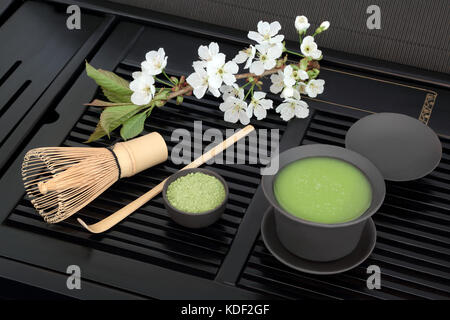 Giapponese Verde matcha tè con polvere e salute bevanda in tazza con frusta, stick agitatore e molla di fiori di ciliegio sul vassoio nero Foto Stock