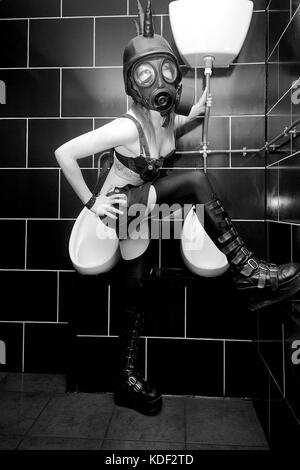 La ragazza di moda alternativa includente una maschera a gas in gents bagni in un night club ubicazione Foto Stock