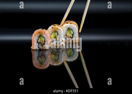 Close up di sushi rotoli farciti con avocado e polpa di granchio isolata su uno sfondo nero Foto Stock