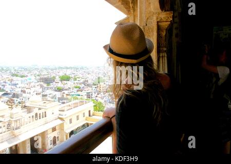 Viaggiatore femmina guarda attraverso una finestra a Udaipur City Palace di Udaipur, India Foto Stock