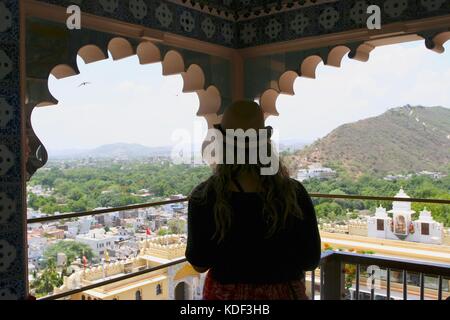 Viaggiatore femmina guarda attraverso una finestra a Udaipur City Palace di Udaipur, India Foto Stock