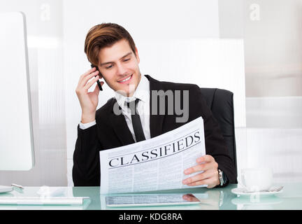Giovane imprenditore parlando al cellulare quotidiano di lettura Foto Stock