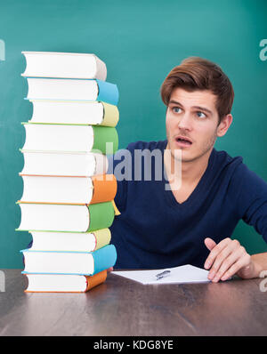 Ritratto di un maschio scioccato studente guardando alla pila di libri Foto Stock