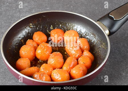 Glassato al miele carotine con sale marino e timo in una padella su un grigio Sfondo astratto. Il mangiare sano concetto. il digiuno cibo. pasto sano Foto Stock